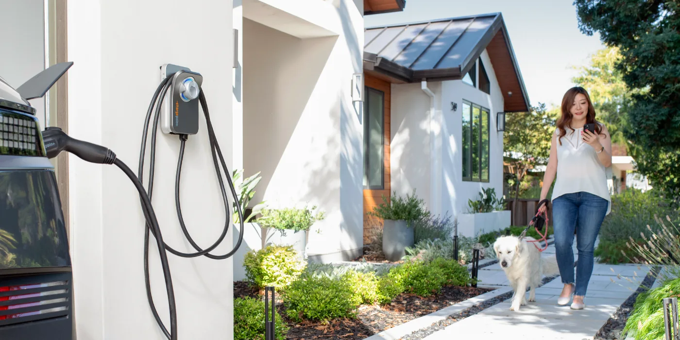 Homeowner walking her dog beside an electric vehicle charging at home